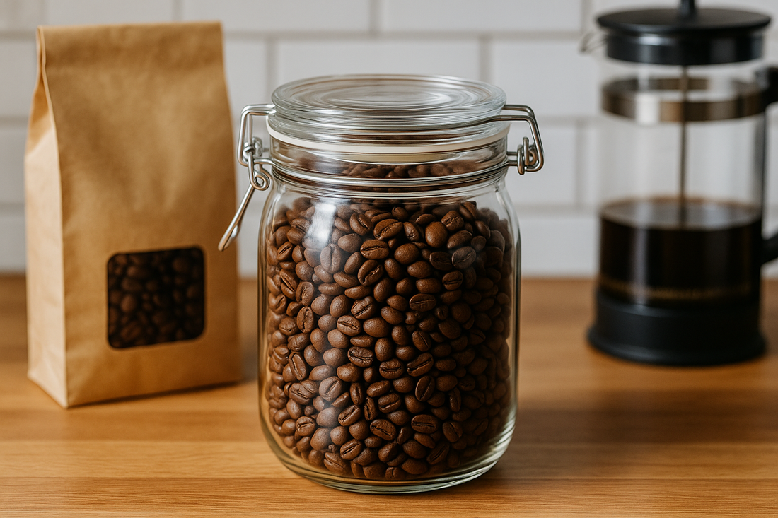 A sealed glass jar filled with roasted coffee beans sits on a wooden countertop next to a kraft paper coffee bag and a French press, illustrating proper coffee storage.